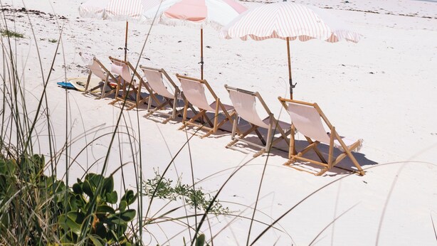 Een strand met wit zand, een rij strandstoelen en gestreepte parasols.