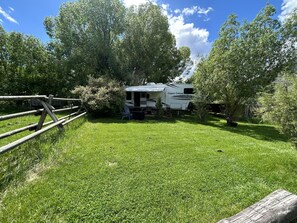 A white RV named 'Copper Canyon' parked in a grassy area with a wooden fence and trees in the background. - Unique Yellowstone Camping Glamping Getaway.   RV on Solo Sight w/ Full Hookups (Gardiner)