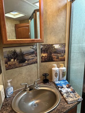 A bathroom with a sink, hand soap dispenser, and Pantene Moisture shampoo and conditioner. - Unique Yellowstone Camping Glamping Getaway.   RV on Solo Sight w/ Full Hookups (Gardiner)