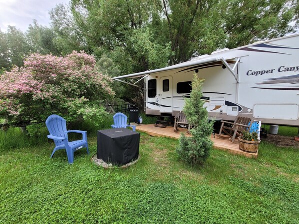 A recreational vehicle with a covered patio area, blue chairs, and a small table. - Unique Yellowstone Camping Glamping Getaway.   RV on Solo Sight w/ Full Hookups (Gardiner)