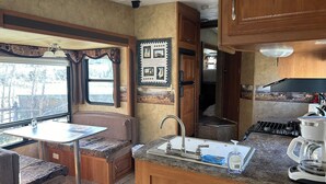 A compact RV kitchen with a sink, stove, and a dining area with a table and bench.