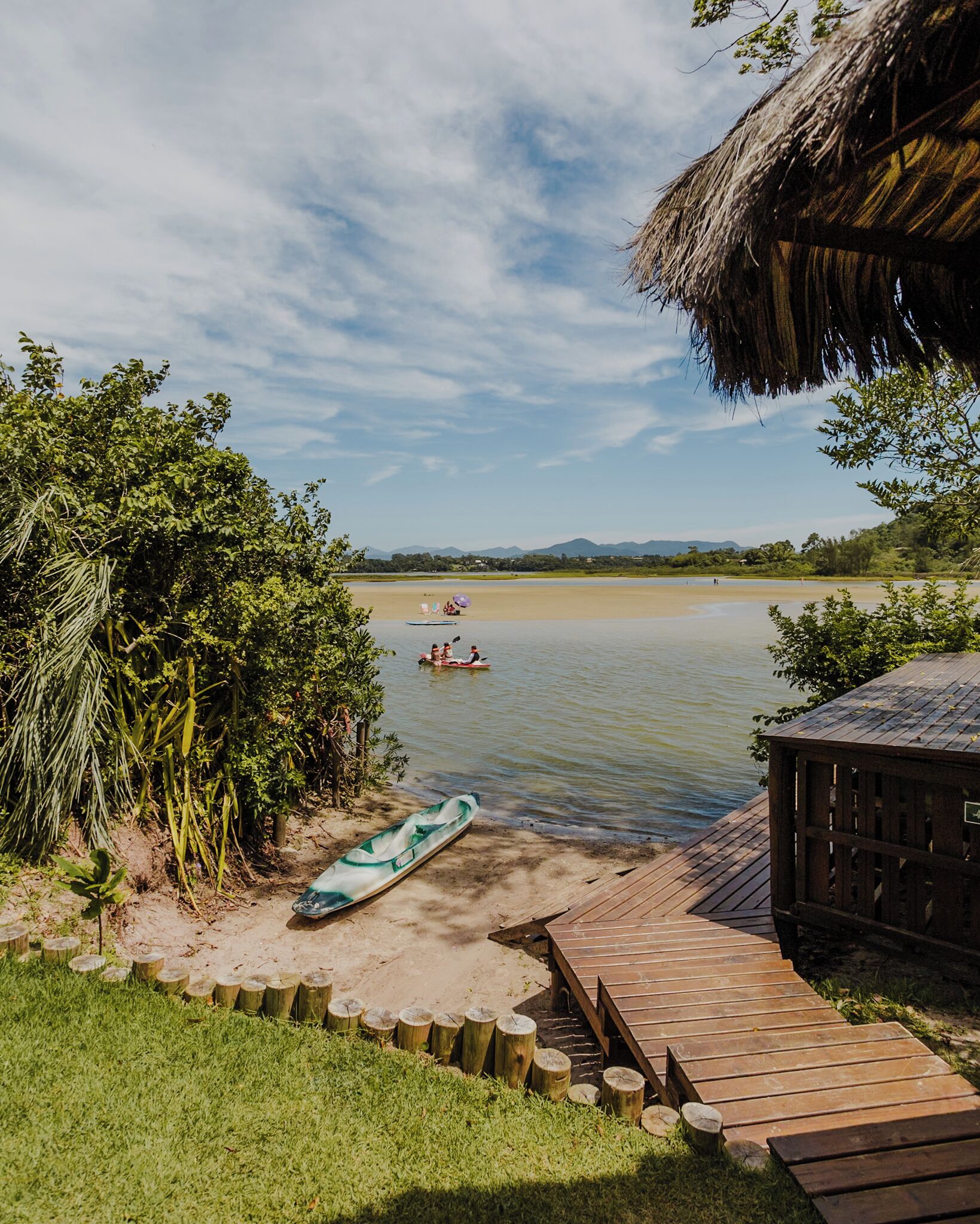 A wooden dock leading to a calm lake with a thatched-roof structure on the right.