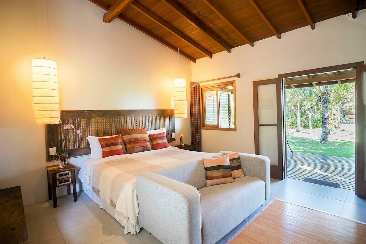 A bedroom with a large bed, two bedside lamps, a wooden headboard, and a view of a garden through a sliding door.