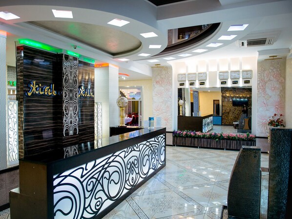A hotel reception area with a modern design, featuring a reception desk, a clock displaying multiple time zones, and a decorative wall with floral patterns.