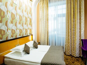 A hotel room with a large bed, a headboard, a window with curtains, and a patterned carpet.