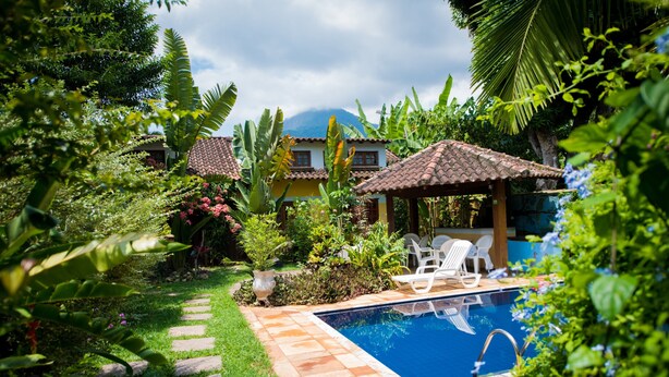A swimming pool surrounded by lush greenery, a tiled deck, and a small gazebo. - Pouso Sambaquis (Ilhabela)