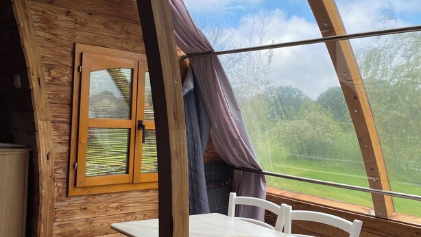 Un interior de madera acogedor con una mesa y sillas, una ventana con cortinas y vistas a vegetación.