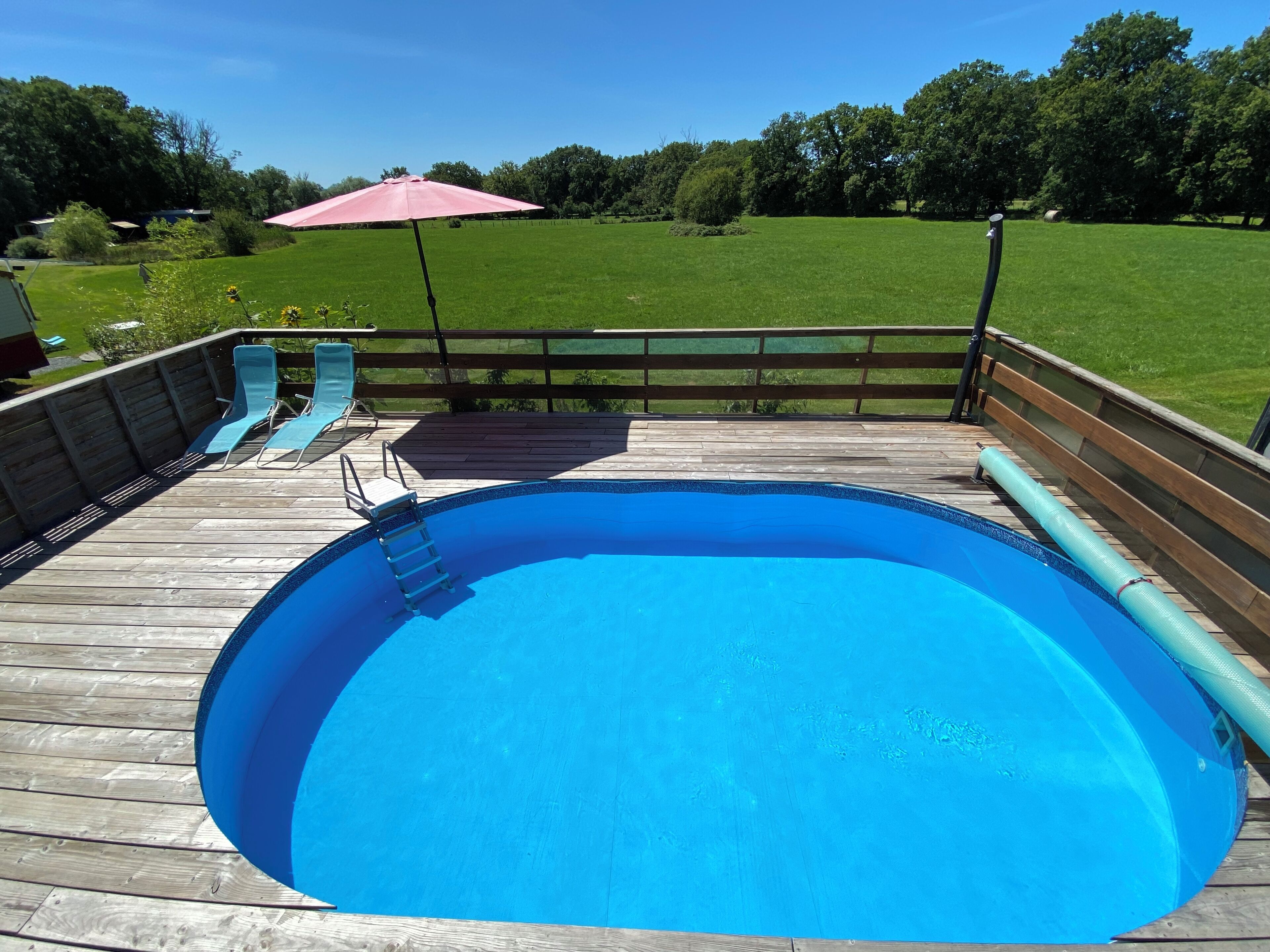 A swimming pool with a wooden deck, a slide, and a red umbrella.