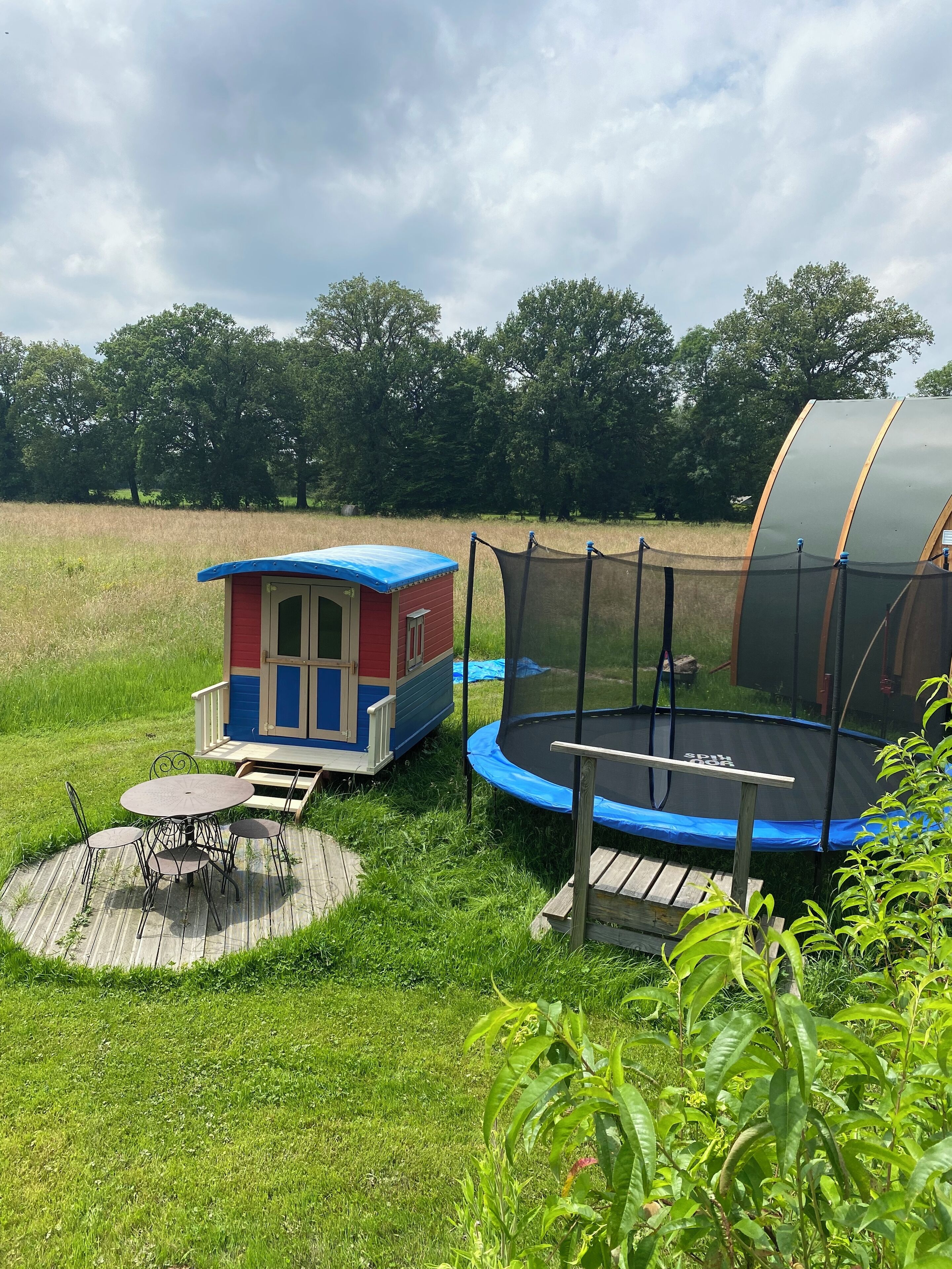 Ein Spielplatz mit einem kleinen Häuschen, Trampolin und Picknicktisch in einer grünen Wiese.
