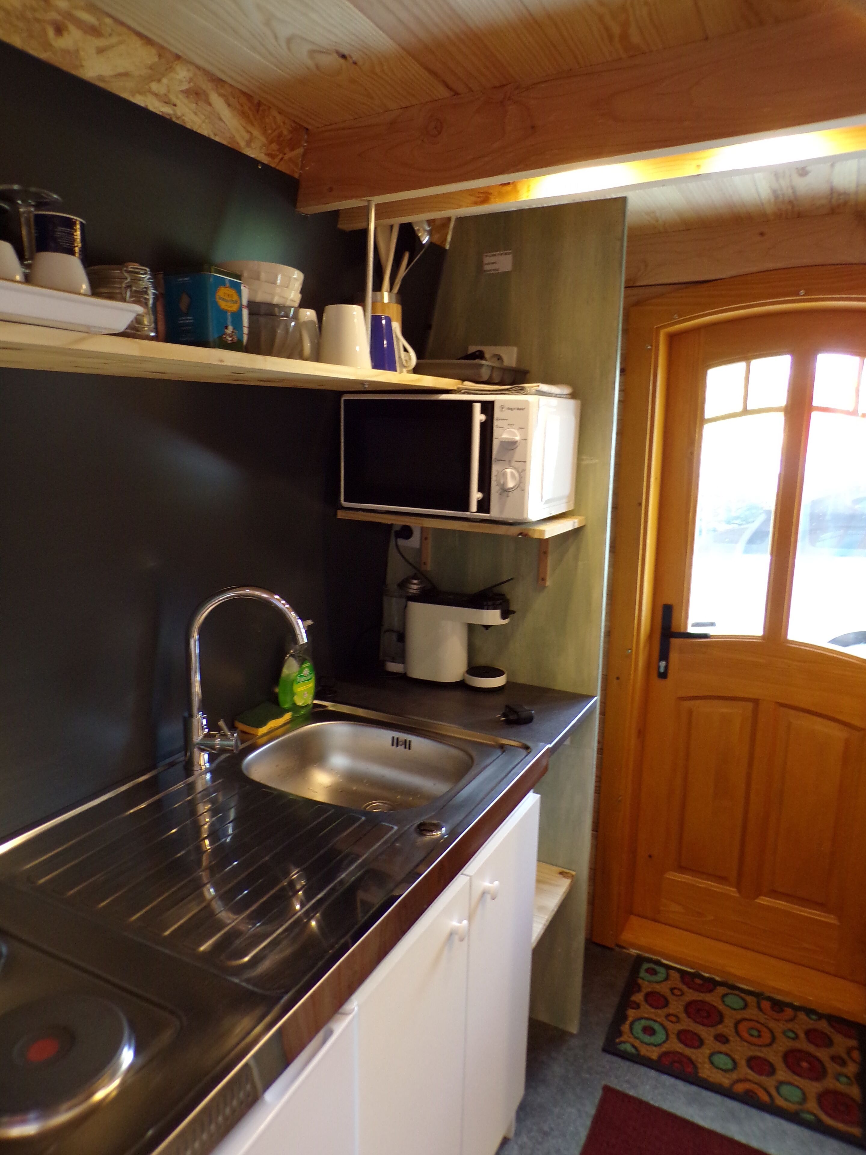 A compact kitchen with a stainless steel sink, a microwave, and a wooden door.
