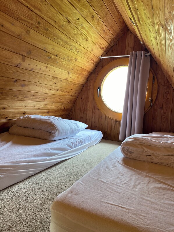 A cozy attic bedroom with wooden walls, a round skylight, and two neatly made beds.