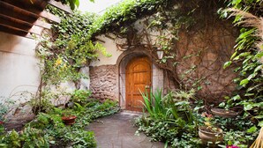 A stone pathway leading to a wooden door surrounded by lush greenery and potted plants. - Unique House in Historical Center (Cuzco)