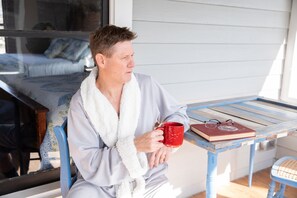 A person sitting at a table with a book and a red mug, holding a pair of glasses. - Red Gate Inn LLC (McKinney)