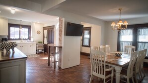 Une cuisine spacieuse avec un coin repas, un plancher en bois, des meubles de cuisine blancs et un téléviseur à écran plat fixé au mur.