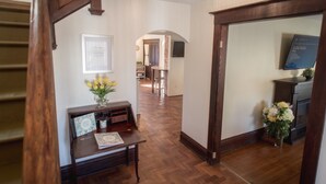 Un couloir au plancher de bois, avec un bureau et un vase de fleurs, qui mène à une salle à manger.