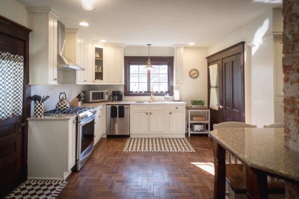 Una cocina con armarios blancos, piso de madera en patrón de espiga y una isla central, además de un área de comedor con mesa y sillas.