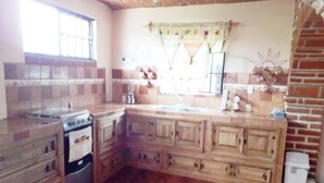A kitchen with wooden cabinets, a stove, and a window with curtains. - Beautiful country house (Jocotepec)