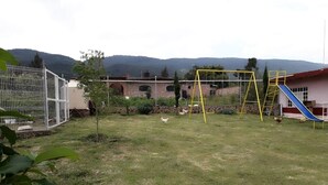 A grassy yard with a playground, a fenced area, and a building with a red roof. - Beautiful country house (Jocotepec)