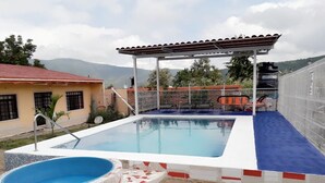 A swimming pool with a tiled deck, a covered seating area, and a view of the surrounding landscape. - Beautiful country house (Jocotepec)