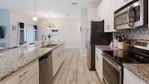 A modern kitchen with granite countertops, stainless steel appliances, and a central island. - Home Away from Home by VillaDirect (Davenport)