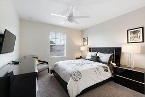 A modern bedroom with a bed, bedside tables, a desk, a chair, a ceiling fan, and a window. - Home Away from Home by VillaDirect (Davenport)