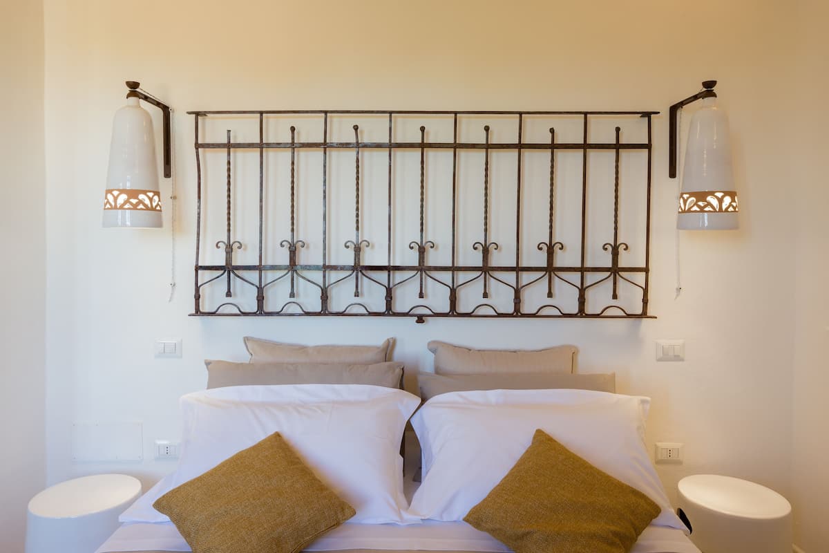 A hotel room with a large bed, two bedside tables, a decorative metal headboard, and two wall-mounted lamps.