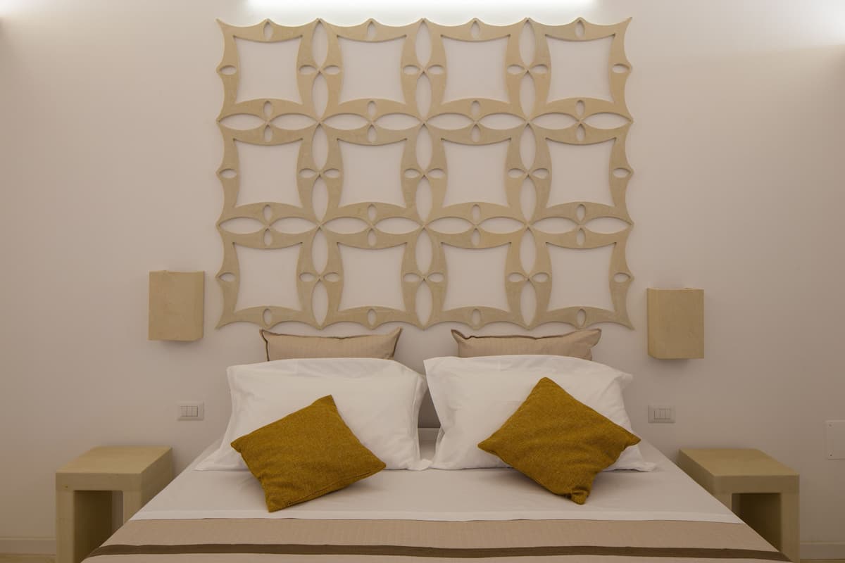A neatly made bed with two pillows, a decorative headboard, and bedside tables.