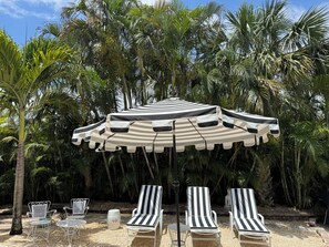A beachside lounge with striped lounge chairs and a striped canopy umbrella.