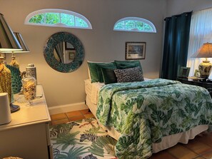 A bedroom with a bed, two windows, a mirror, and a lamp.