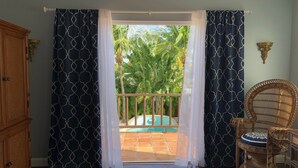 A room with a view of a pool and palm trees, a wicker chair, and a wooden cabinet.