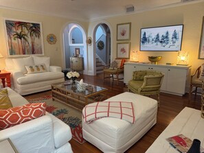 A living room with a sofa, armchairs, a coffee table, and a television. There are framed pictures on the walls and a decorative bowl on the coffee table.