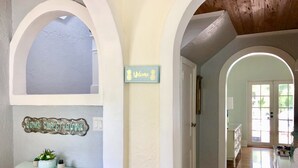 A hallway with a light blue wall, a welcome sign, a rustic wooden ceiling, and a door leading to another room.