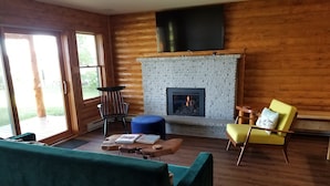 Una sala de estar acogedora con chimenea, paredes de madera, un sofá verde y un sillón amarillo.