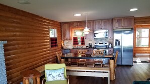 Una cocina acogedora de estilo rústico con paredes de madera, una isla central con taburetes altos y un refrigerador de acero inoxidable.