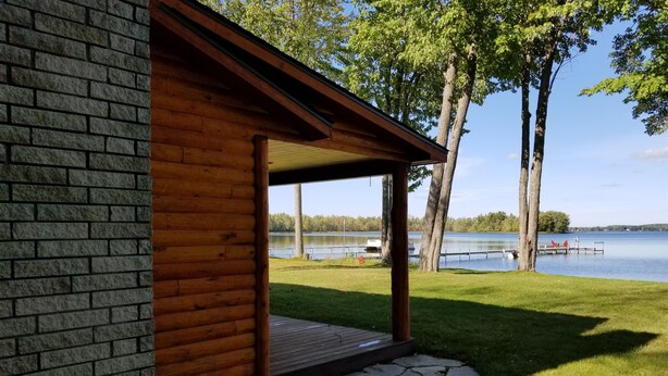 Una cabaña de madera con base de piedra, un porche cubierto y vista a un lago y un muelle.
