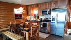 Una cocina estilo cabaña de madera con una mesa de comedor, sillas, una banca, un refrigerador, una estufa y un microondas.