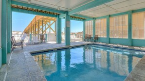 Piscina interior com vista clara para a praia, área ao redor da piscina com cadeiras e um espaço coberto com deck de madeira.