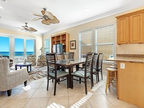 A spacious living area with a large dining table, comfortable seating, and a view of the ocean. - 🥳 Early Bird Sale. First 2! Wits End, West. 6BR. Pool. Awesome 2nd floor beach walkover! (Gulf Shores)