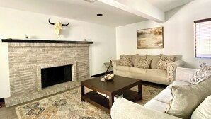 A living room with a brick fireplace, a sofa, a coffee table, and a decorative skull on the wall. - Spacious Mesa Oasis with FREE Heated POOL (Mesa)