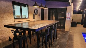 A bar area with a long table and multiple stools, a dartboard, and a sign indicating no photography. - Spacious Mesa Oasis with FREE Heated POOL (Mesa)