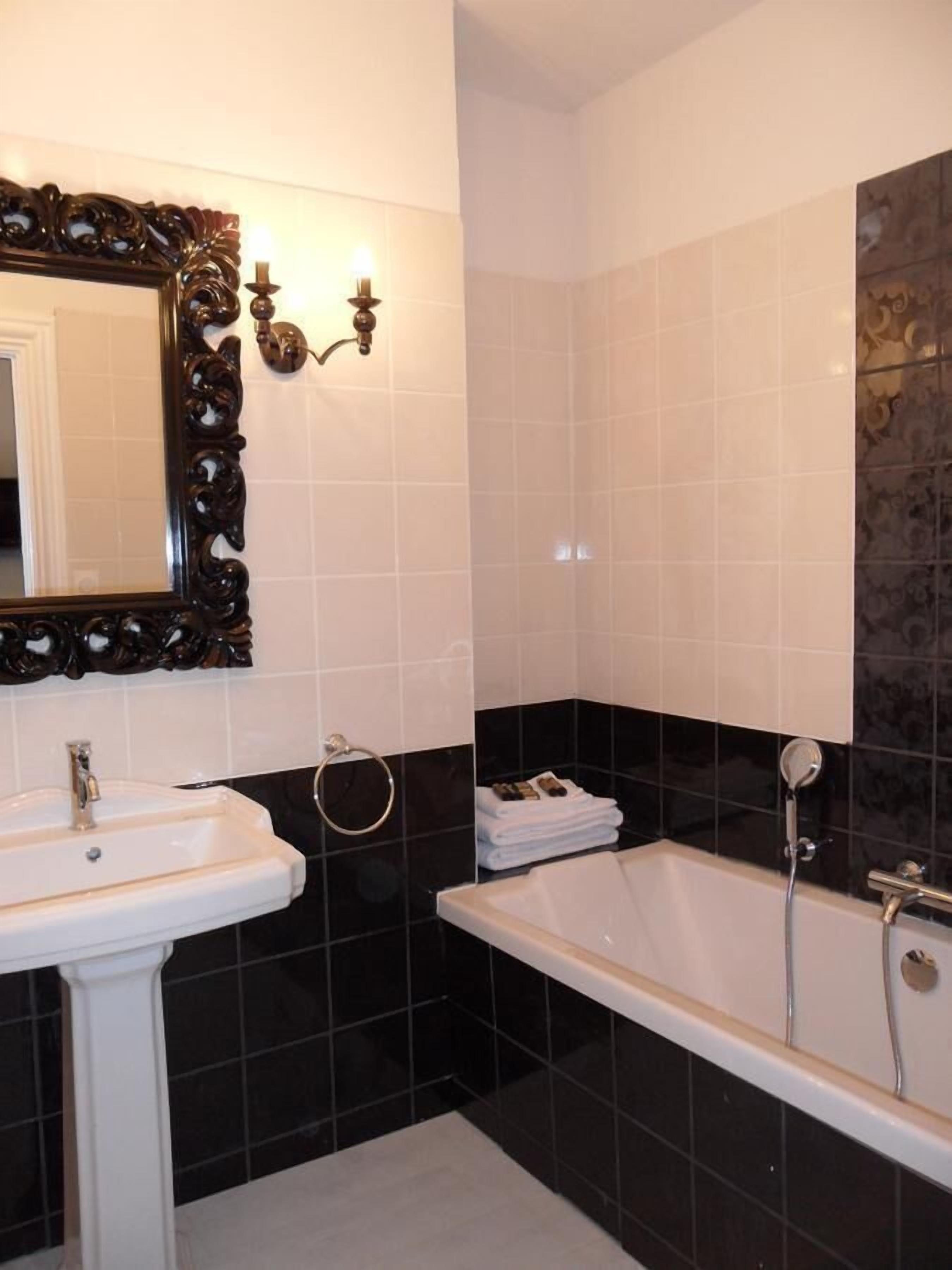 A bathroom with a white sink, a large mirror with an ornate frame, a bathtub, and black and white tiled walls.