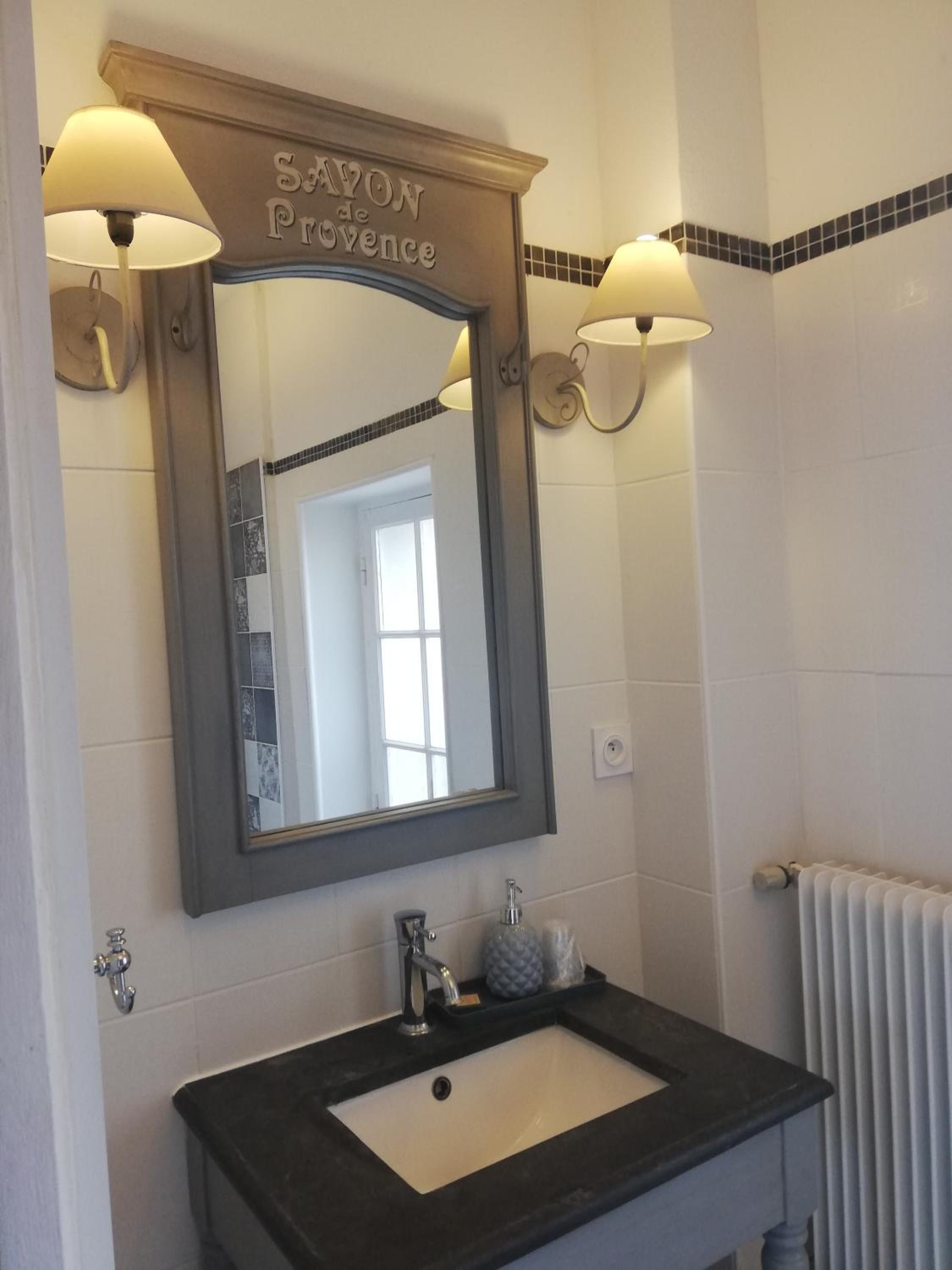 A bathroom with a large mirror, two wall-mounted lights, a sink with a soap dispenser, and a towel rack.