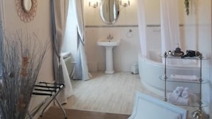 A bathroom with a bathtub, a sink, a mirror, a chandelier, and a glass shelf with toiletries. - Chateau les 4 saisons (Saint-Cirgues-sur-Couze)