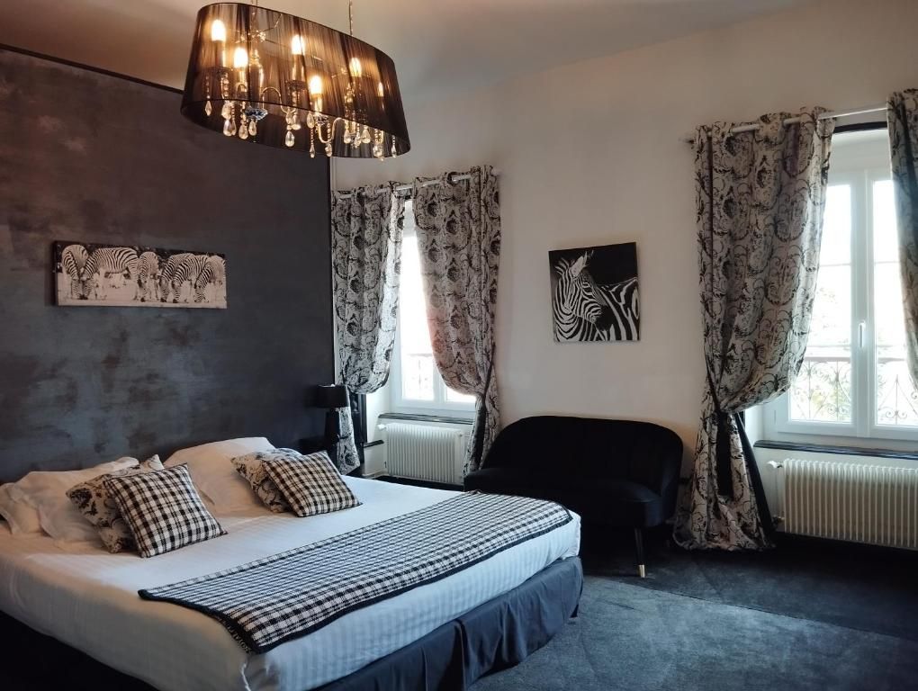 Een slaapkamer met een bed, een zwarte stoel, een kroonluchter, gordijnen met een patroon en kunst aan de muren.