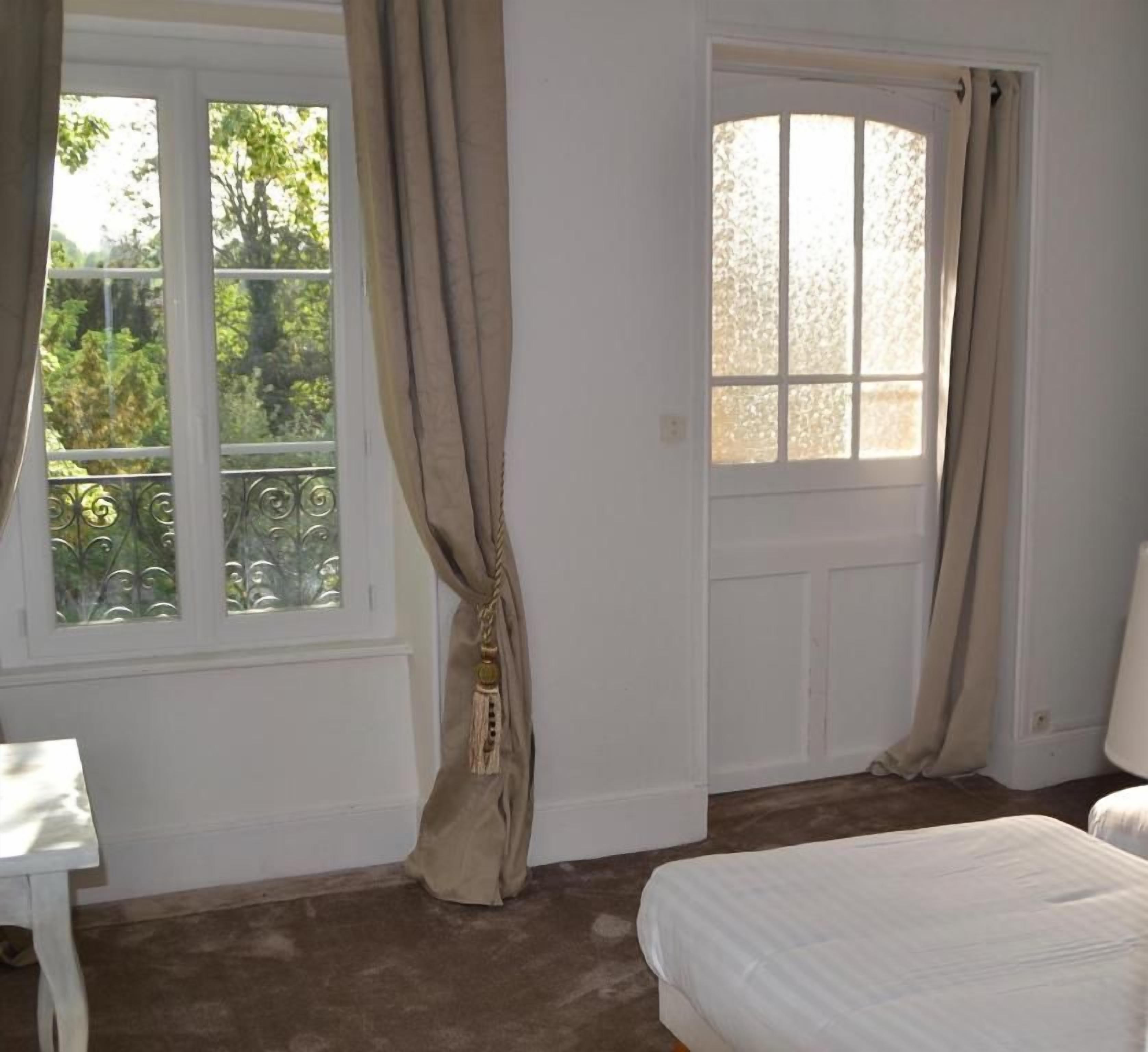 A bedroom with a bed, a window with curtains, a door, and a small table.