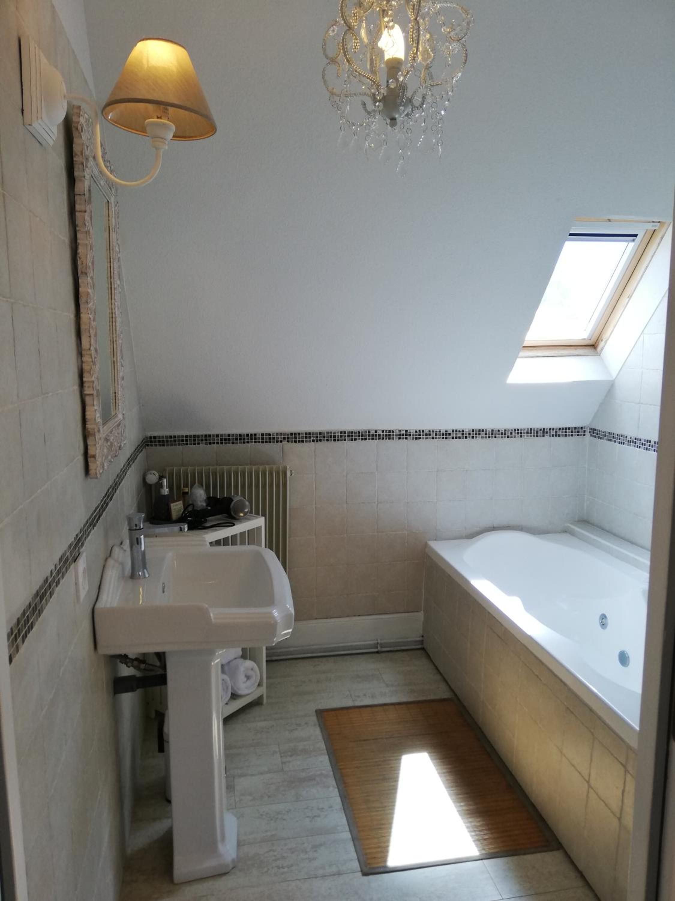 A bathroom with a sink, a bathtub, a shower, a chandelier, and a skylight.