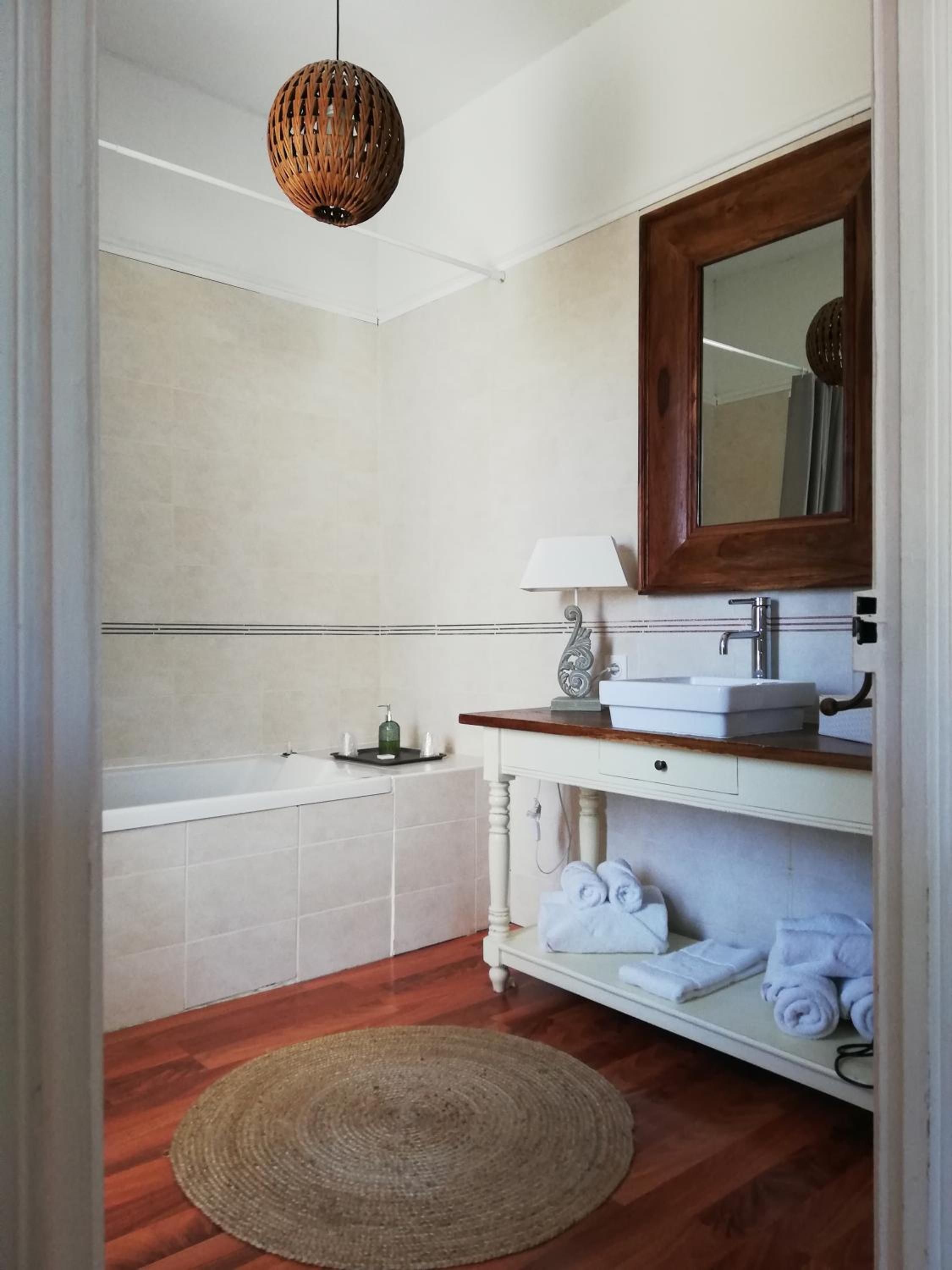 Un baño con bañera, lavamanos con espejo, toallero y un tapete tejido en el suelo.