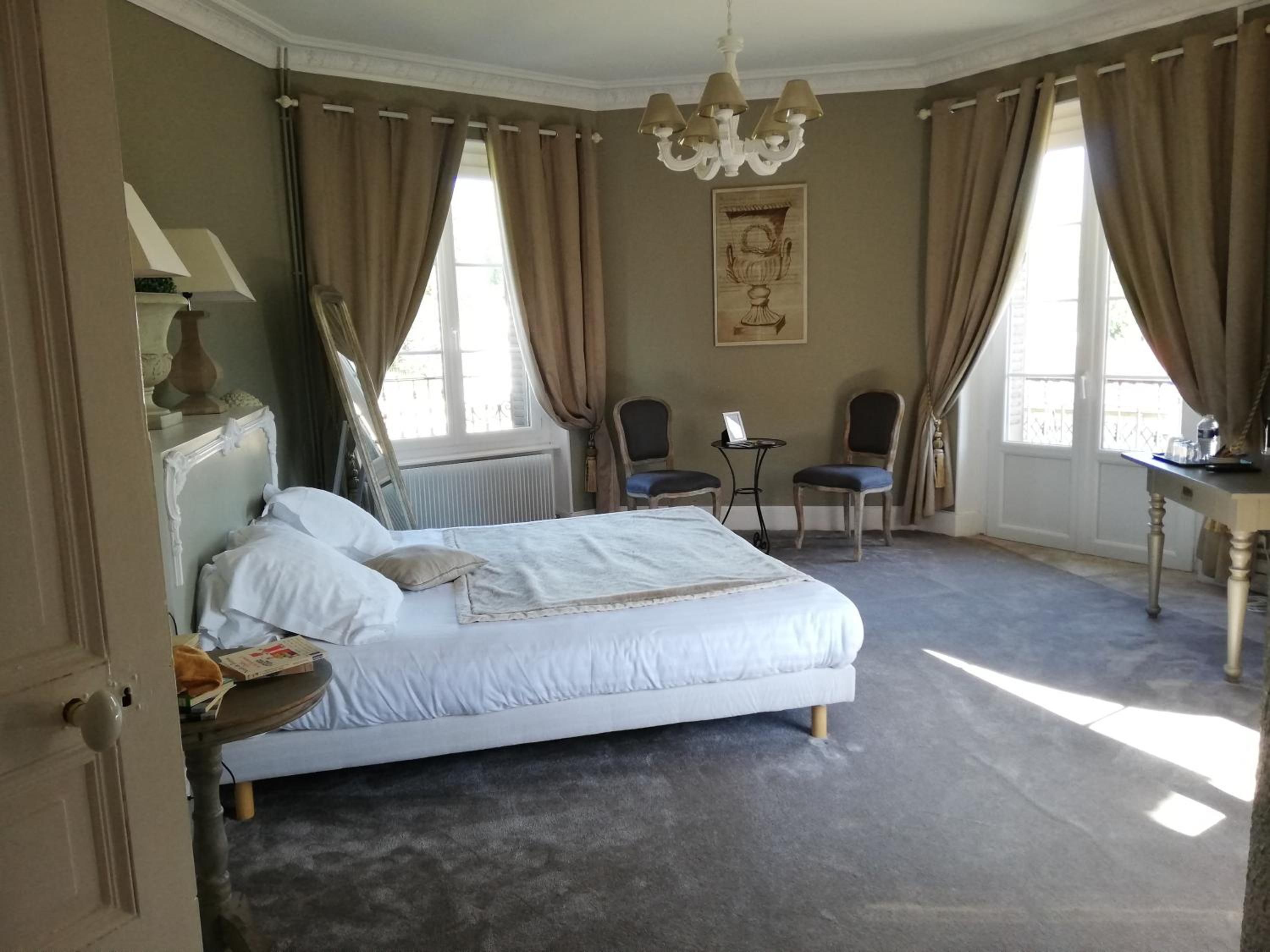 A hotel room with a large bed, two chairs, a small table, and a chandelier.
