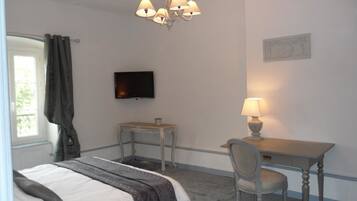 A hotel room with a bed, a desk, a chair, a television, and a lamp.