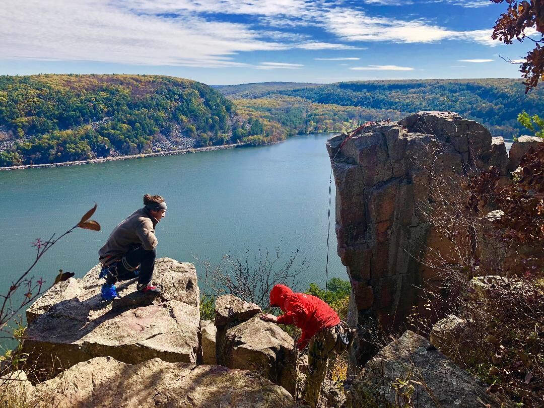 A person in a red jacket climbing a rocky cliff overlooking a lake.